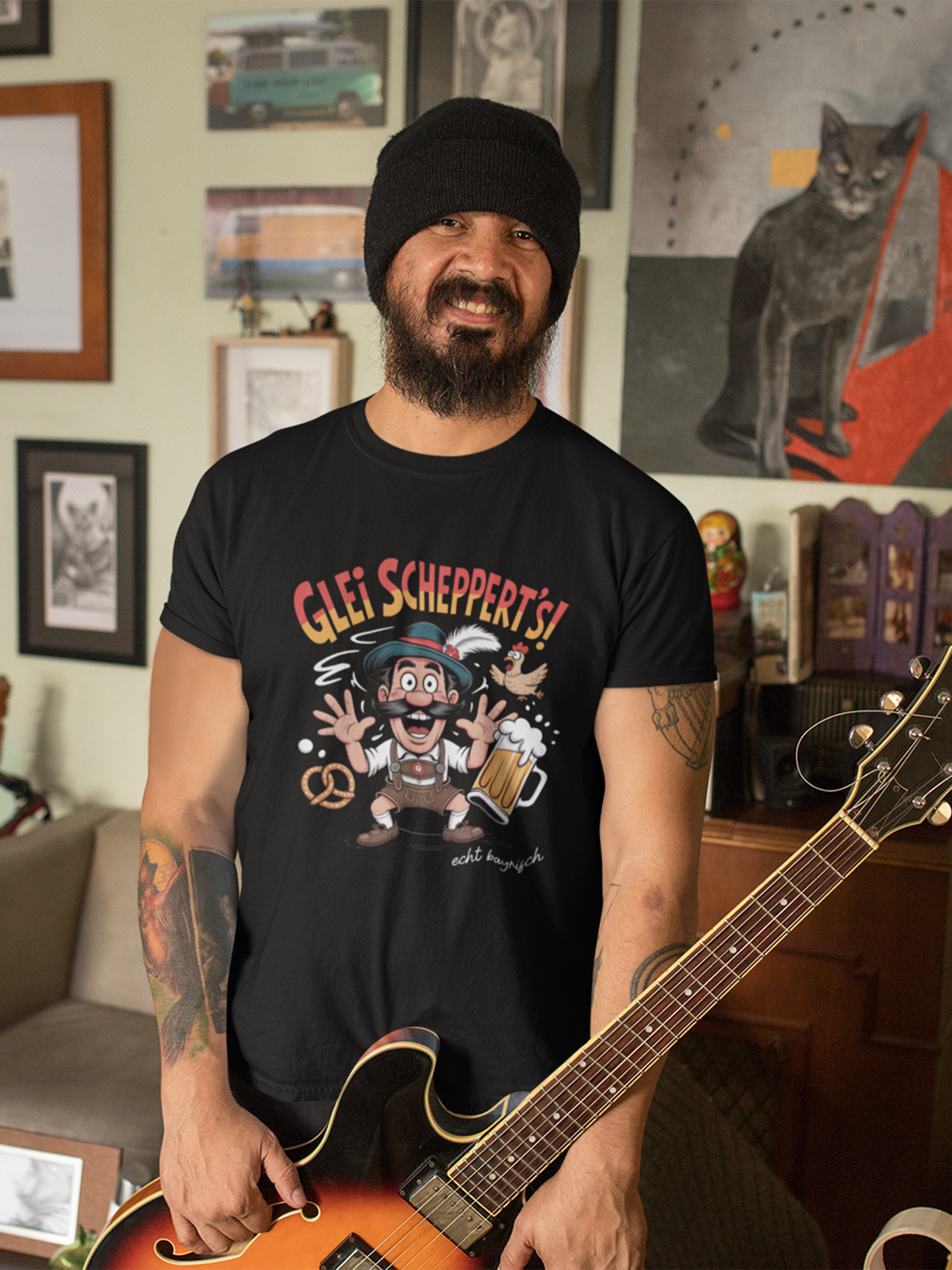 Mann mit Bart und Gitarre trägt schwarzes T-Shirt mit Fun-Motiv „Glei scheppert’s“, Oberkörperansicht