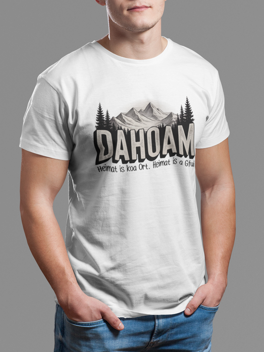 Junger Mann trägt weißes T-Shirt mit Sepia-Bergmotiv und großem „Dahoam“-Schriftzug, Oberkörperansicht