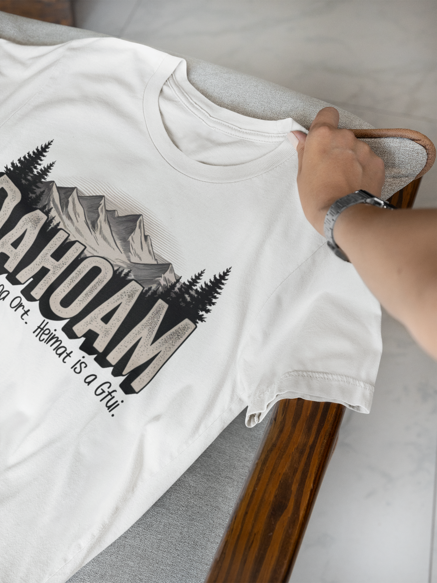 Weißes T-Shirt, liegend, mit großem Schriftzug „Dahoam“ und Bergmotiv in Sepia