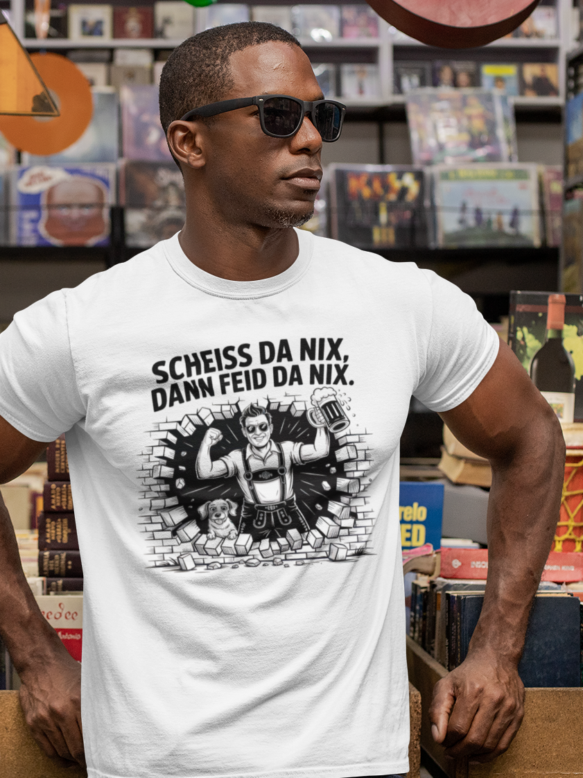 Junger schwarzer Mann mit Sonnenbrille, trägt weißes T-Shirt mit dem Spruch „Scheiß da nix, dann feid da nix“, Oberkörperansicht. Im Hintergrund CDs im Regal.