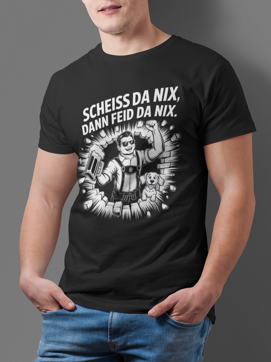 Junger Mann trägt ein schwarzes T-Shirt mit weißem Text „Scheiß da nix, dann feid da nix“ und Comic-Motiv eines Bayern mit Hund und Wand. Oberkörperansicht.