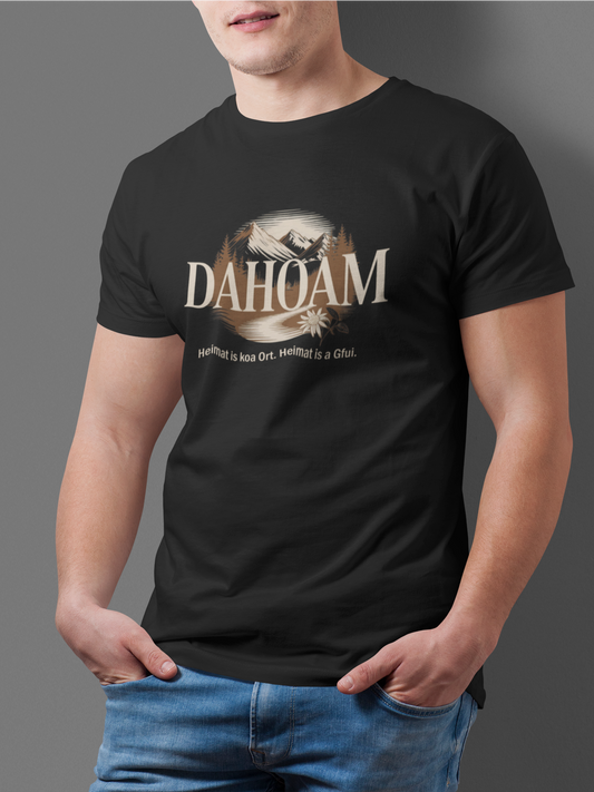 Junger Mann trägt schwarzes T-Shirt mit Bergmotiv in Sepia und Text „Dahoam. Heimat is koa Ort. Heimat is a Gfui.“, Oberkörperansicht