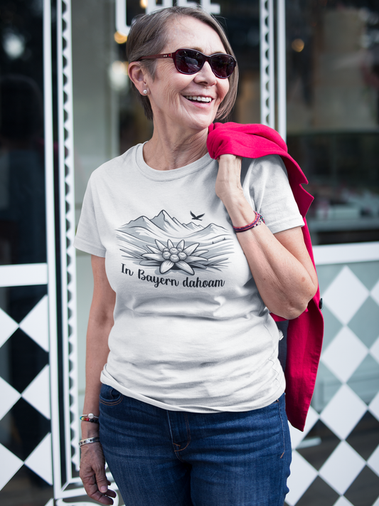 Frau mit Sonnebrille trägt weißes T-Shirt mit Bergpanorama, Edelweiß und Text „In Bayern Dahoam“, Oberkörperansicht