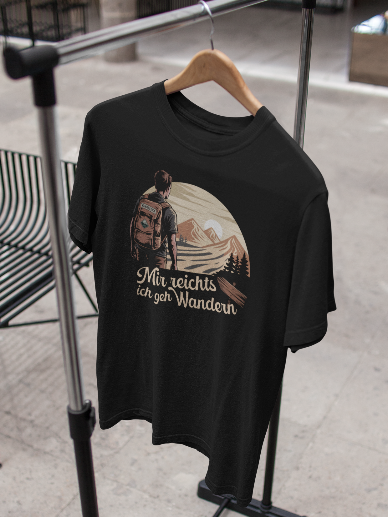 Schwarzes T-Shirt mit sepiafarbenem Motiv „Mir reicht’s, ich geh wandern“ auf Kleiderbügel an Kleiderständer