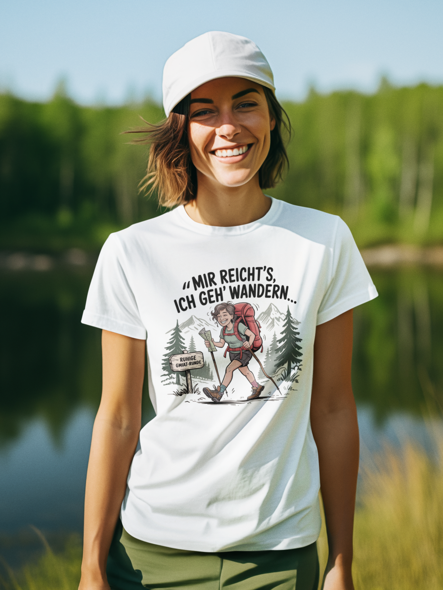 Junge Frau trägt weißes T-Shirt mit dem Aufdruck „Mir reicht’s – ich geh wandern“, Oberkörperansicht, Blick nach vorn. Im Hintergrund ein See und Wald.