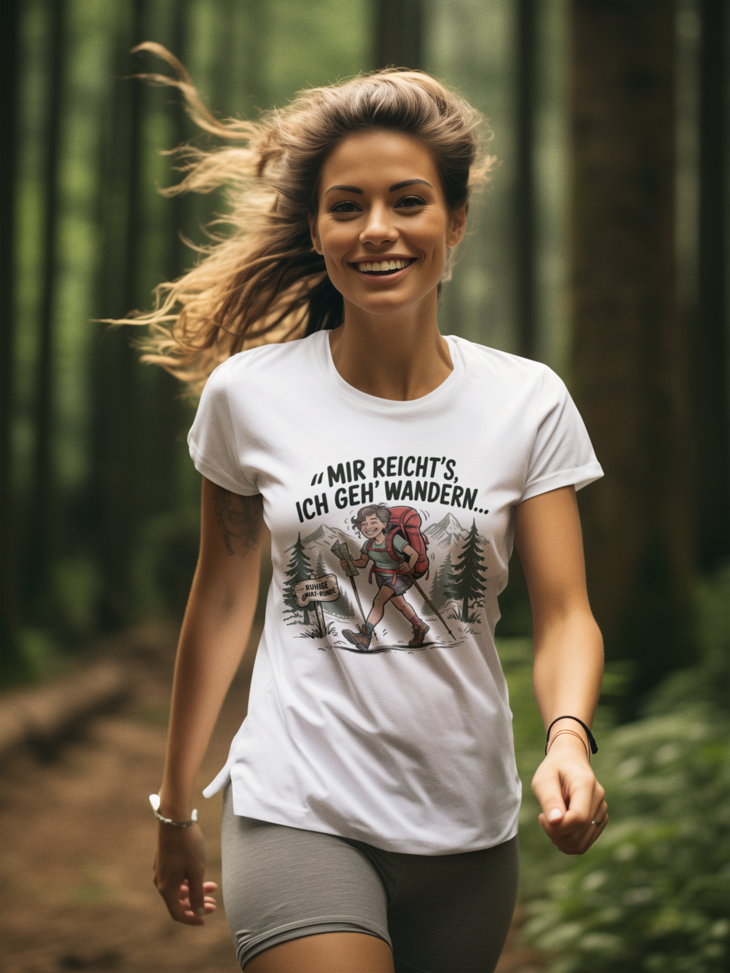 Junge Frau trägt weißes T-Shirt mit dem Aufdruck „Mir reicht’s – ich geh wandern“, Oberkörperansicht, Blick nach vorn, laufend, im Hintergrund Wald.