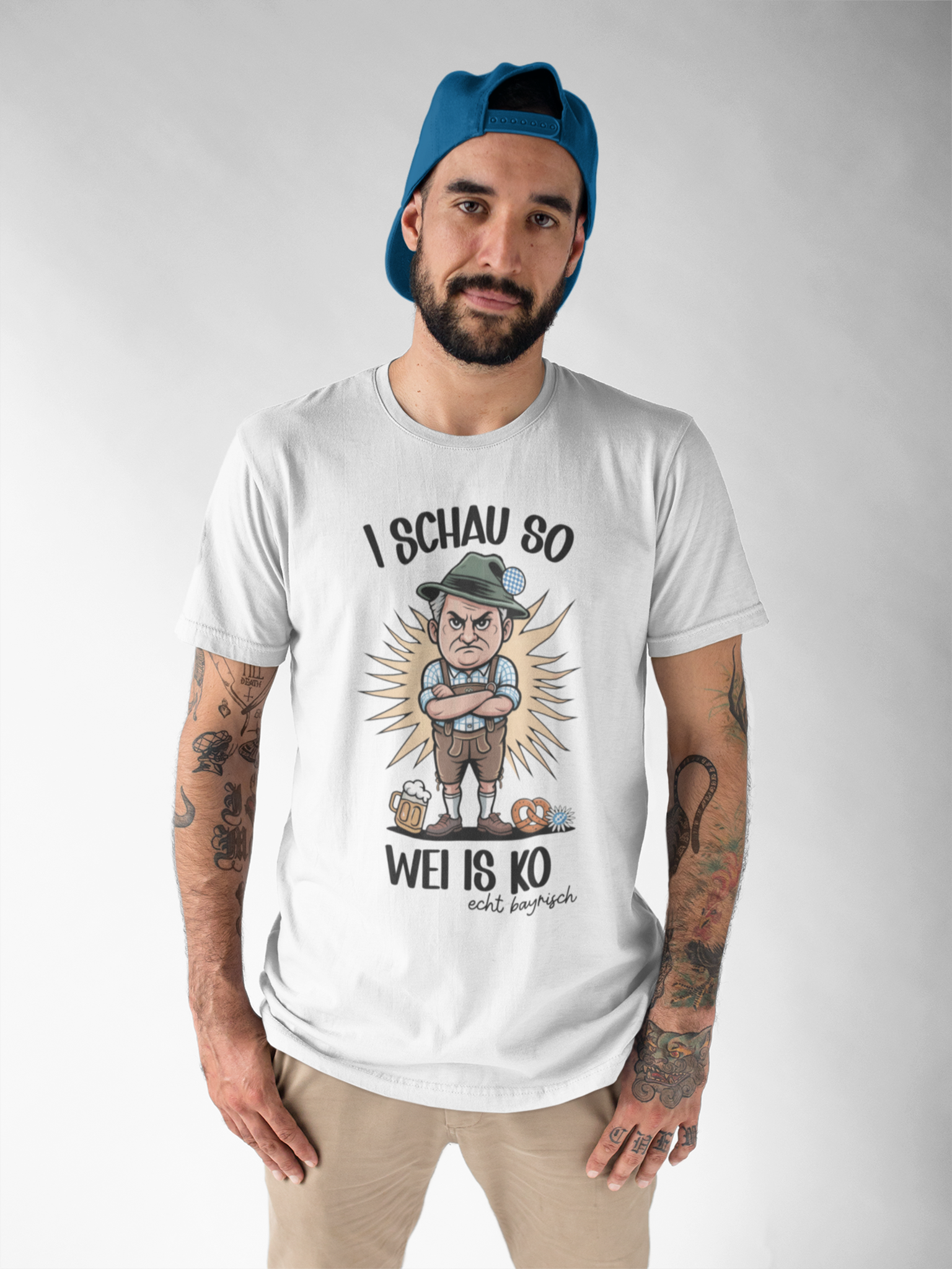 Junger Mann trägt weißes T-Shirt mit grimmigem Bayer-Motiv und Spruch „I schau so wei is ko“, Oberkörperansicht