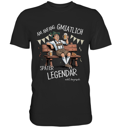 Schwarzes T-Shirt mit der Aufschrift „Bayrisch am Anfang gmiatlich, später legendär“ und farbigem Motiv eines Bayers mit Maß auf Bank