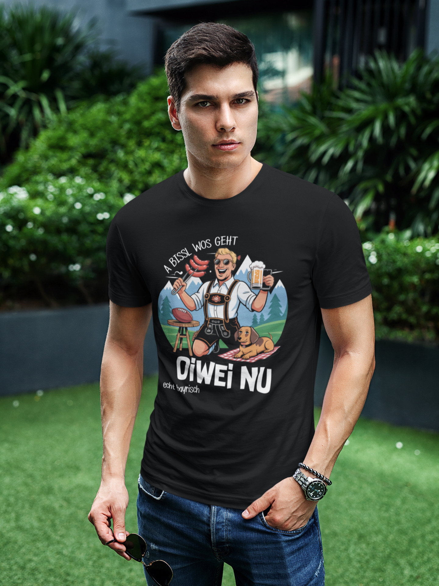 Junger Mann trägt schwarzes T-Shirt mit Bratwurst-und-Maß-Motiv und Spruch „A bissl wos geht oiwei nu“, Oberkörperansicht