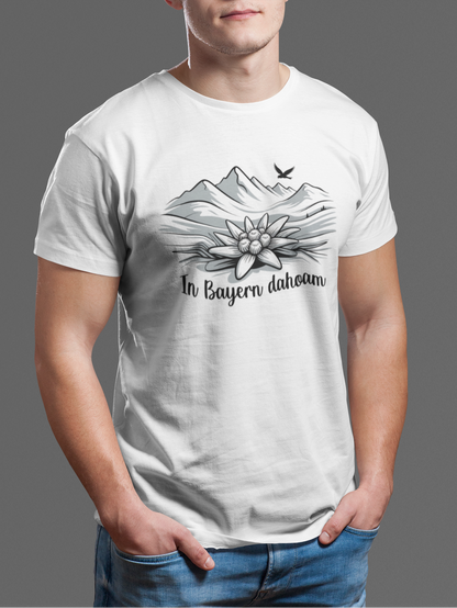 Junger Mann trägt weißes T-Shirt mit Bergpanorama, Edelweiß und Text „In Bayern Dahoam“, Oberkörperansicht