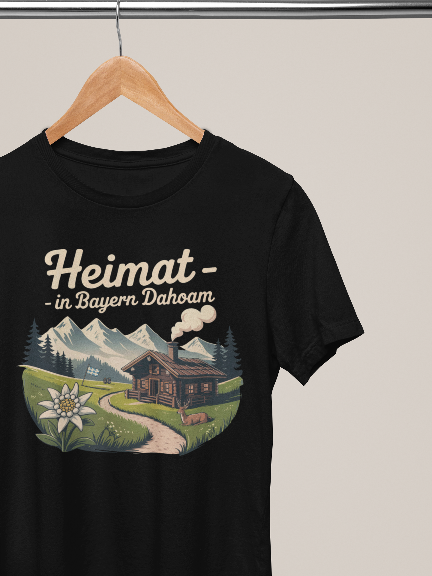 Schwarzes T-Shirt mit Bergmotiv, Almhütte und Text „Heimat – In Bayern dahoam“ auf Kleiderbügel 
